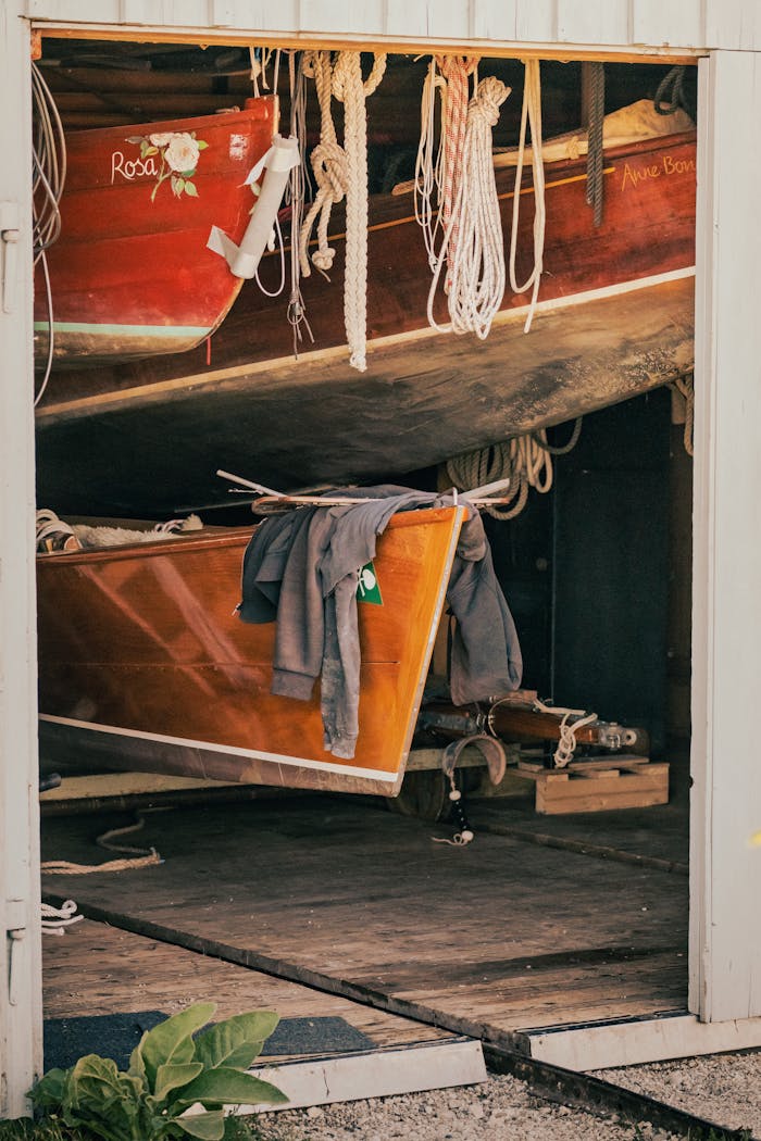 A view of classic wooden boats stored in a rustic shed, draped with ropes and a jacket.
